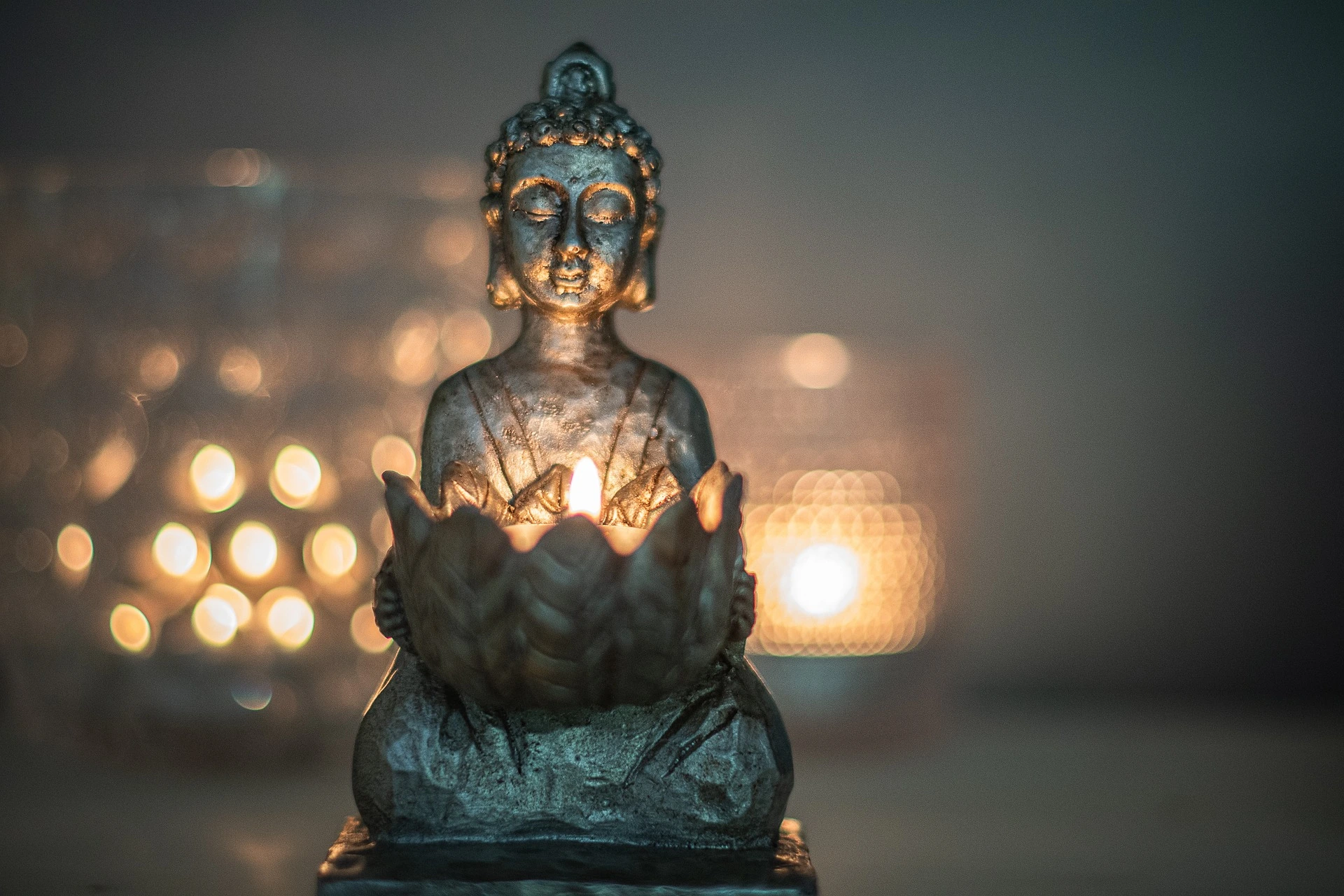 Eine braune Buddhafigur mit Kerzen im Hintergrund.